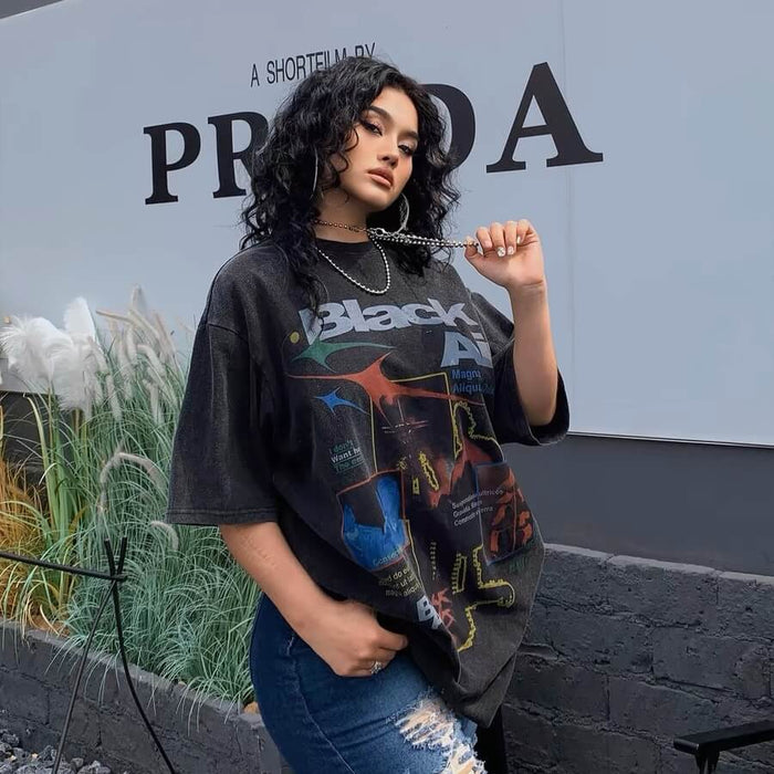 Woman wearing an oversized graphic t-shirt and ripped jeans standing in front of a PRADA sign.