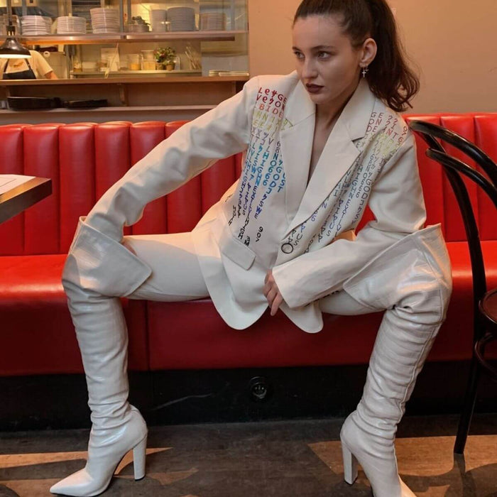 Woman wearing a stylish white pantsuit with colorful embellishments, sitting in a restaurant booth.